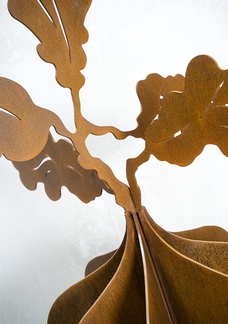 lose-up detail of an outdoor sculpture showing 3mm thick layers of Corten metal slotted together with oak leaf details. Brief Description: This image provides a close-up view of an outdoor sculpture made from 3mm thick layers of Corten metal. The layers are intricately slotted together, featuring detailed oak leaf designs. The rust finish and craftsmanship highlight the sculpture's rustic elegance and artistic precision.
