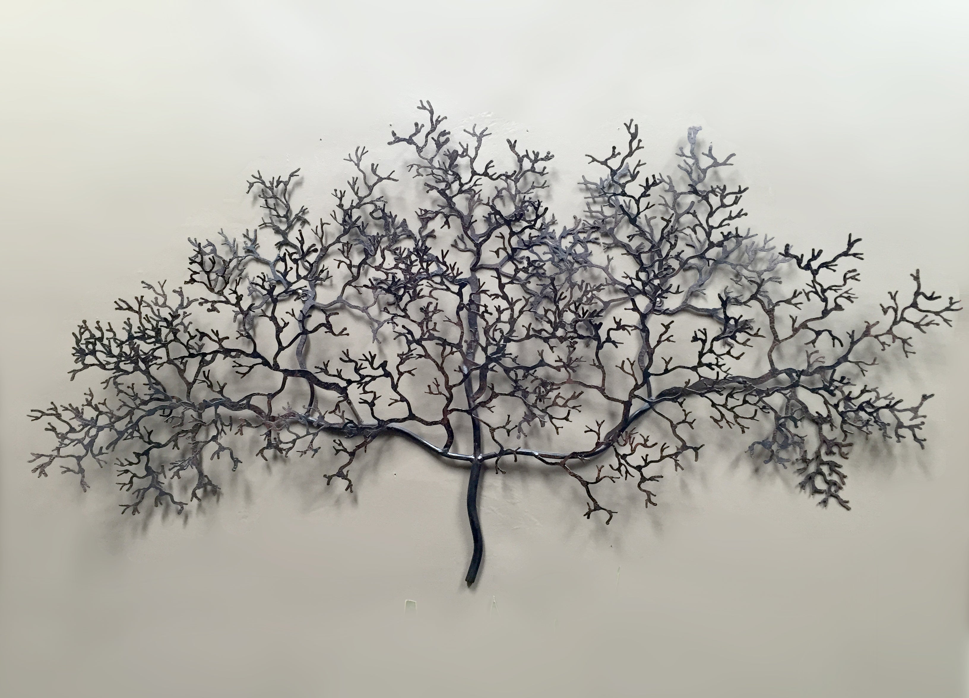 Hand-made tree branch-like wall art made from crushed metal, displayed against a concrete rendered wall.
