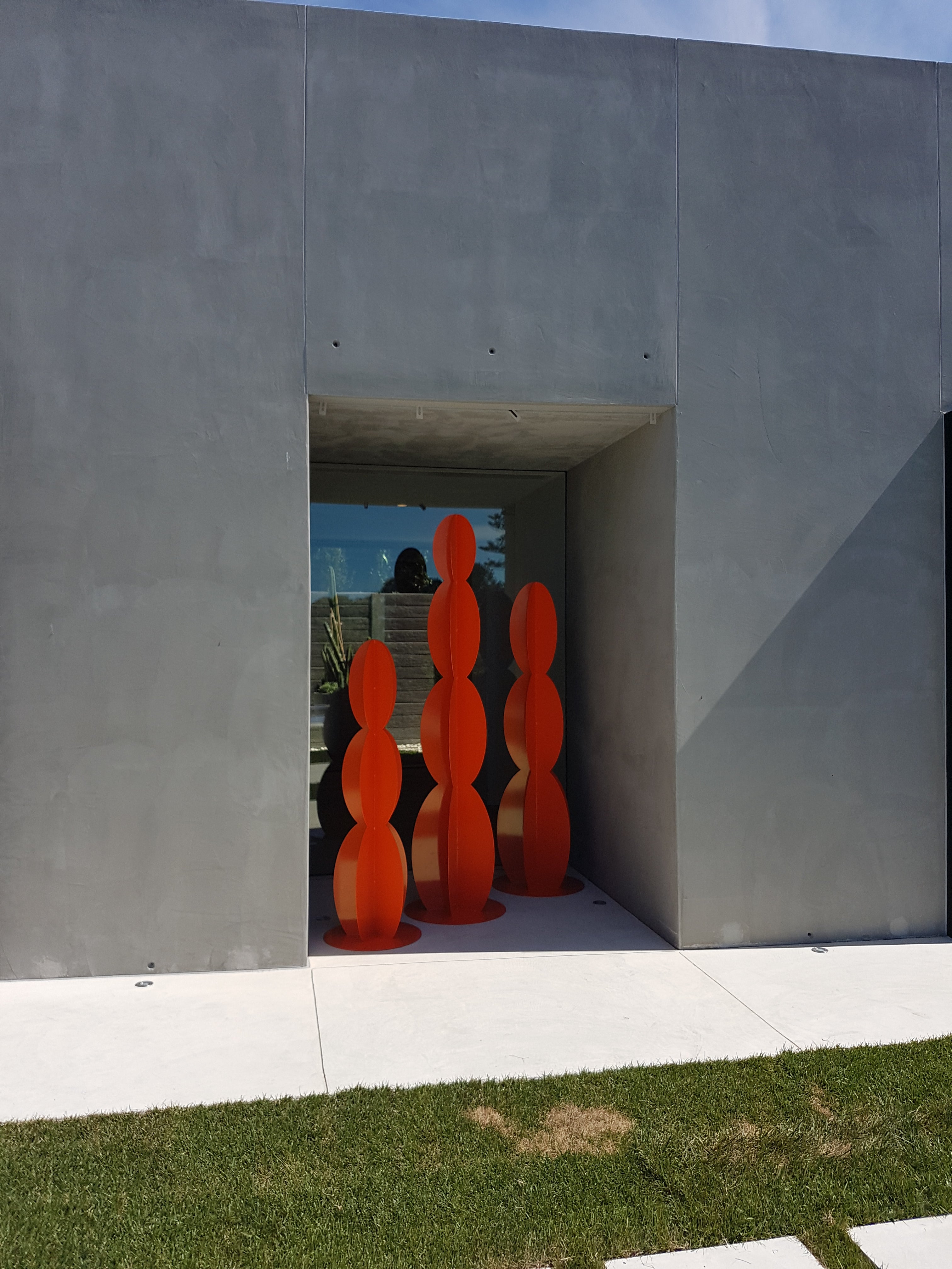  "Entanglements Red Cacti Sculpture: A collection of red cacti sculptures artfully displayed within a concrete alcove. The sculptures are framed by the alcove and complemented by a window offering a view of the surrounding coastal landscape. This minimalist mid-century design sculpture enhances the aesthetic appeal of the coastal house."
